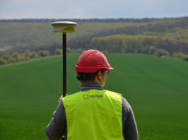 egy férfi földmérő eszközt tart, Lechneres láthatósági mellényt visel