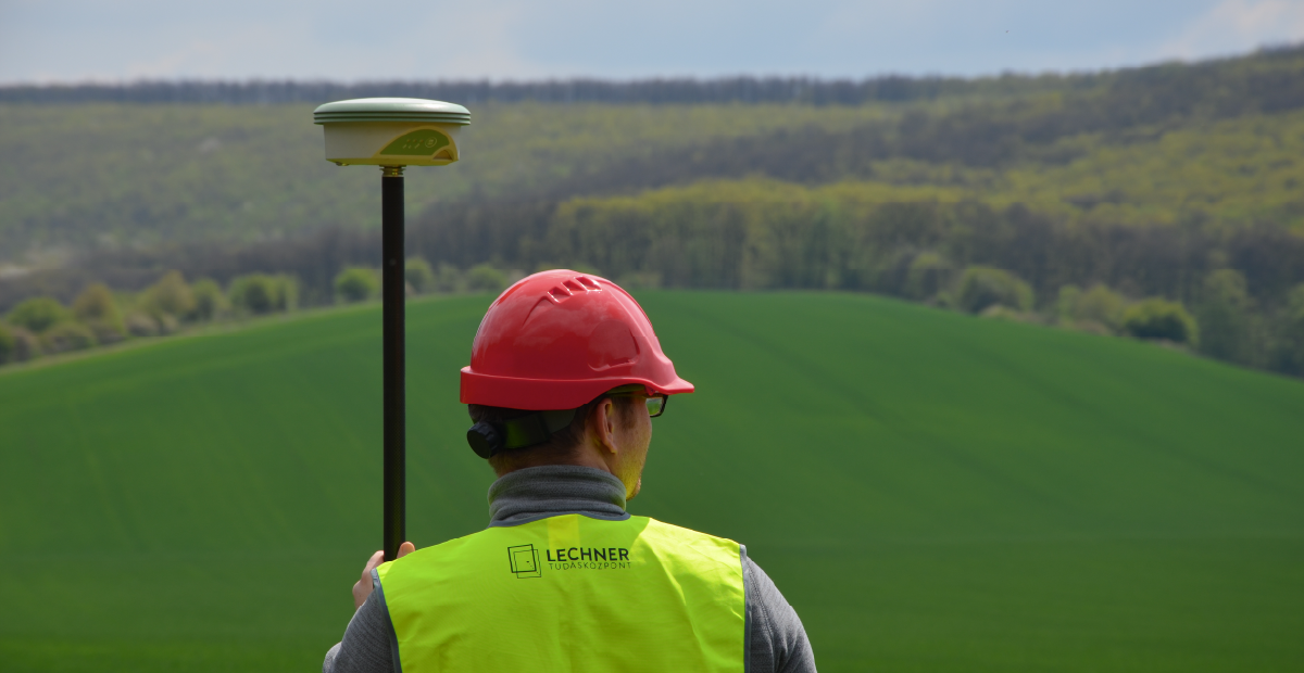 egy férfi földmérő eszközt tart, Lechneres láthatósági mellényt visel